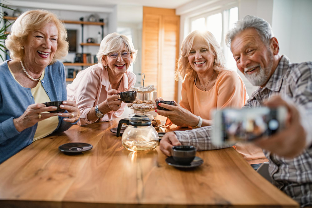 A group of elederly people clicking a selfie while drinking tea.