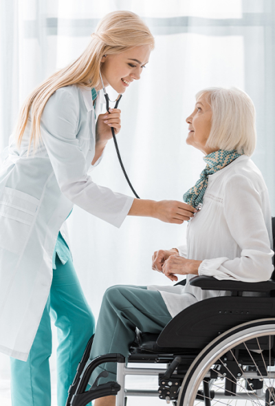 A doctor with stethoscope checking the heart bit of a patient who is sitting on a wheelchair.